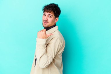 Kafkasyalı genç adam mavi arka plan noktalarında izole edilmiş başparmak uzakta, gülüyor ve kaygısız.