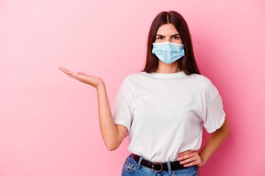 Pembe arka planda izole edilmiş virüs maskesi takan beyaz bir kadın bir avuç içinde fotokopi alanı ve belinde başka bir el tutuyor..