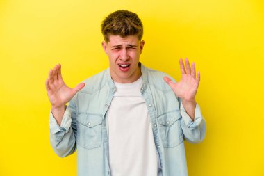 Sarı arka planda izole edilmiş genç beyaz adam öfkeyle bağırıyor..