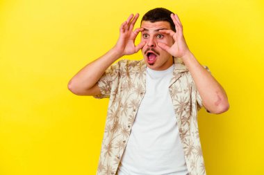 Sarı arka planda izole edilmiş genç beyaz adam bir başarı fırsatı bulmak için gözlerini açık tutuyor..