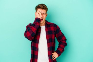 Mavi arka planda izole edilmiş genç beyaz adam yüzünün yarısını palmiye ile kaplayarak eğleniyor..