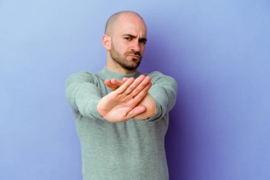 Kafkasyalı genç kel adam mor arka planda izole edilmiş elini uzatmış, dur işareti gösteriyor, bu da seni engelliyor..