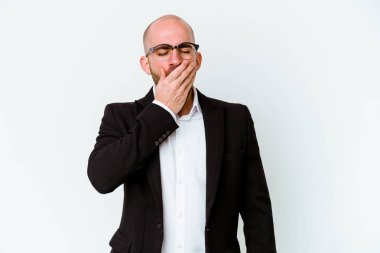 Genç, beyaz, kel bir adam mavi arka planda izole edilmiş esniyor. Ağzı eliyle kapatan yorgun bir hareket sergiliyor..