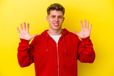 Sarı arka planda izole edilmiş genç beyaz adam on numarayı elleriyle gösteriyor..