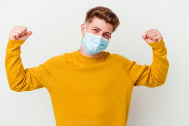 Koronavirüs maskesi takan genç adam beyaz arka planda kadınsı gücün sembolü olan kollarla güçlü bir hareket gösteriyor.