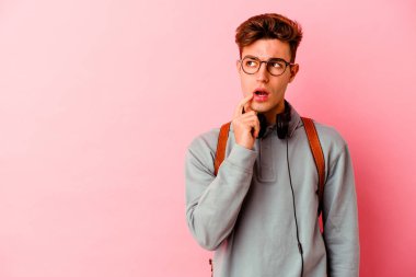 Pembe arka planda izole edilmiş genç bir öğrenci şüpheli ve şüpheci bir ifadeyle yana bakıyor..