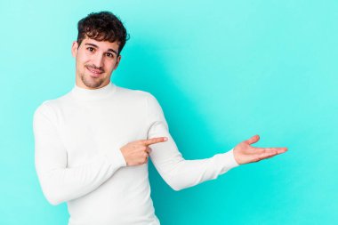 Kafkasyalı genç adam mavi arka planda izole edilmiş. Elinde palmiye ağacının bir kopyası olduğu için heyecanlı..