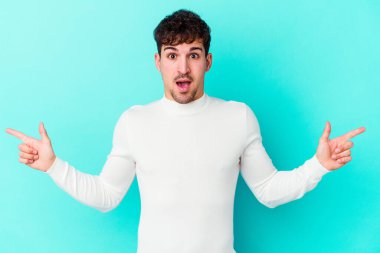 Mavi arka planda izole edilmiş genç beyaz adam farklı kopya alanlarını gösteriyor, birini seçiyor, parmaklarıyla gösteriyor.