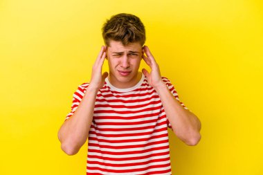 Sarı arka planda izole edilmiş genç beyaz bir adam parmaklarıyla kulaklarını kapatıyor, gürültülü bir ortam yüzünden stresli ve çaresiz..
