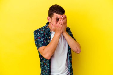 Sarı arka planda izole edilmiş genç beyaz adam parmaklarıyla gözünü kırp korkmuş ve gergin..