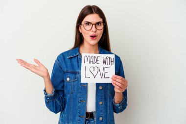 Beyaz arka planda izole edilmiş aşk levhası taşıyan beyaz bir kadın gülümsüyor ve başparmağını kaldırıyor.