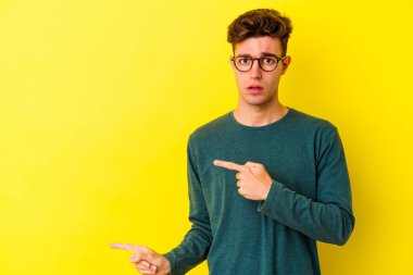 Sarı arka planda izole edilmiş genç beyaz adam işaret parmağıyla fotokopi alanını işaret ederek şok oldu..