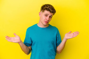Kafkasyalı genç adam sarı arka planda izole edilmiş. Kafası karışmış ve omuz silkiyor. Kopya alanını tutmak için..