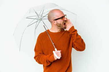 Elinde şemsiyesi olan genç kel bir adam bağırıyor ve avuç içi açık bir şekilde ağzını tutuyor..