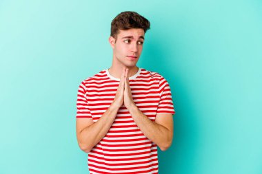 Kafkasyalı genç adam mavi arka planda izole edilmiş dua ediyor, bağlılık gösteriyor, dindar biri ilahi ilham arıyor..