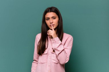 Genç Hintli kadın mavi arka planda izole edilmiş bir şekilde ya sır saklıyor ya da sessizlik istiyor..