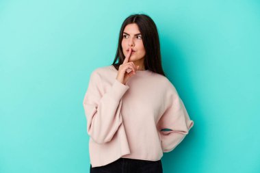 Mavi arka planda izole edilmiş genç beyaz kadın ya sır saklıyor ya da sessizlik istiyor..