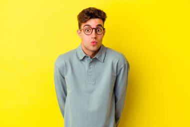 Sarı arka planda izole edilmiş genç beyaz adam omuzlarını silkeliyor ve gözleri açık..