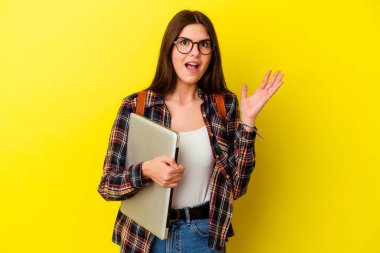 Pembe arka planda dizüstü bilgisayar tutan beyaz bir kadın hoş bir sürprizle karşılaşıyor, heyecanlı ve el kaldırıyor..