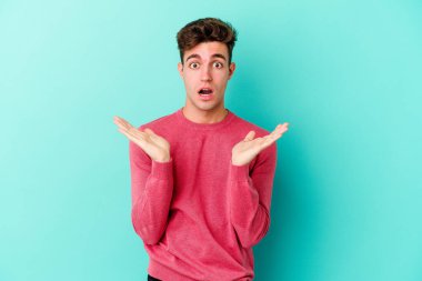 Kafkasyalı genç adam mavi arka planda izole edildi. Şaşırdı ve şok oldu..