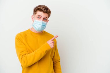 Koronavirüs maskesi takan genç bir adam beyaz arka planda izole edilmiş ve yan tarafı işaret ediyor.