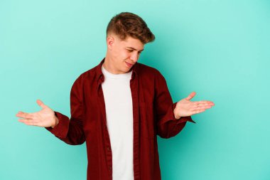 Kafkasyalı genç adam mavi arka planda izole edilmiş. Elinde avuç içi olan bir şey var ve kameraya sunuyor..