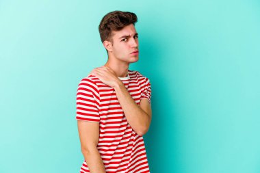 Mavi arka planda izole edilmiş, omuz ağrısı olan genç beyaz bir adam..