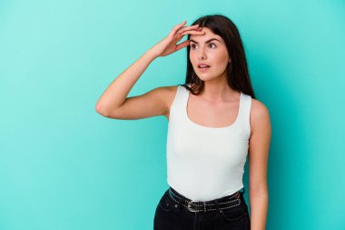 Kafkasyalı genç bir kadın mavi arka planda izole edilmiş, uzaklara bakıyor ve elini alnına koyuyor..