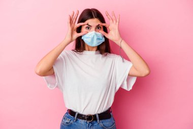 Pembe arka planda izole edilmiş virüs maskesi takan beyaz bir kadın başarı fırsatı bulmak için gözlerini açık tutuyor..