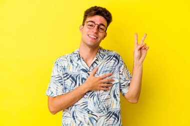 Sarı arka planda izole edilmiş genç beyaz adam yemin ediyor, elini göğsüne koyuyor..