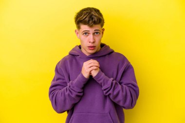 Kafkasyalı genç adam sarı arka planda izole edilmiş şans için dua ediyor, şaşırmış ve ağzını açıp önüne bakıyor..