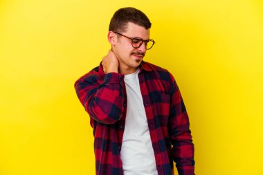 Sarı arka planda izole edilmiş beyaz bir genç. Stresten dolayı boynu ağrıyor. Masaj yapıyor ve elle dokunuyor..