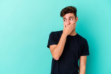 Kafkasyalı genç adam mavi arka planda izole edilmiş. Düşünceli bir şekilde ağzıyla ağzını kapatan bir fotokopi odasına bakıyor..