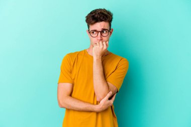 Mavi arka planda izole edilmiş, tırnak yiyen, gergin ve endişeli genç bir beyaz adam..