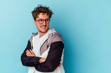 Mavi arka planda izole edilmiş gözlük takan genç beyaz adam gülüyor ve eğleniyor..