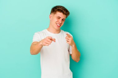 Mavi arka planda izole edilmiş genç beyaz adam parmaklarıyla ön tarafı işaret ediyor..