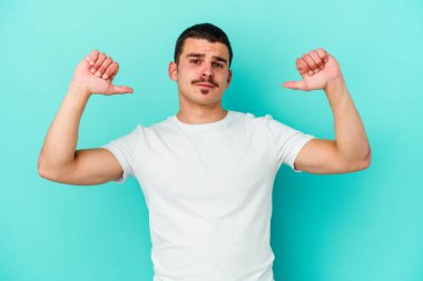Mavi arka planda izole edilmiş genç beyaz adam gururlu ve kendinden emin hissediyor, örnek olarak.