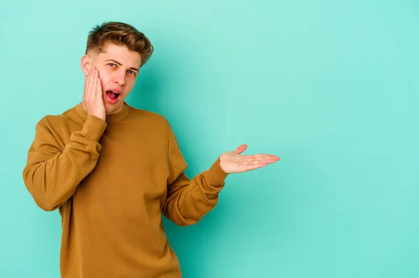 Joven Hombre Caucásico Aislado Sobre Fondo Azul Impresionado Sosteniendo Espacio —  Fotos de Stock