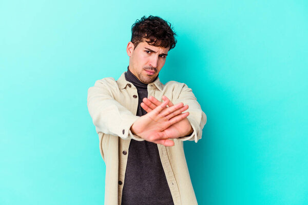 Молодой кавказский человек изолирован на синем фоне стоя с протянутой рукой показывая знак стоп, препятствуя вам.