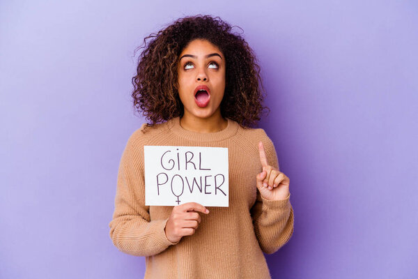 Young African American woman holding a Girl power placard isolated on purple background pointing upside with opened mouth.