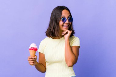 Dondurma yiyen genç melez kadın ellerini çenesinin altında tutuyor ve mutlu bir şekilde yan tarafa bakıyor..