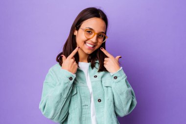 Genç melez kadın yalnız gülüyor, parmaklarıyla ağzını işaret ediyor..