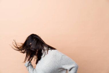 Genç Hintli kadın saçlarını bej arka planda tek başına taşıyor.