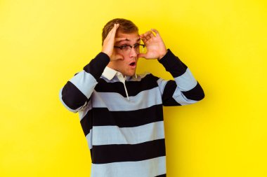 Sarı arka planda izole edilmiş genç beyaz adam bir başarı fırsatı bulmak için gözlerini açık tutuyor..