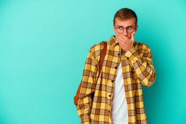 Kafkasyalı genç bir öğrenci mavi arka planda izole edilmiş. Düşünceli bir şekilde bir fotokopi odasına bakıyor. Ağzını eliyle kapatıyor..