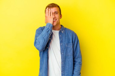 Sarı arka planda izole edilmiş genç beyaz adam yüzünün yarısını palmiye ile örterek eğleniyor..