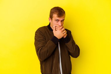 Sarı arka planda izole edilmiş genç beyaz adam elleri endişeli bir şekilde ağzı örtüyor..