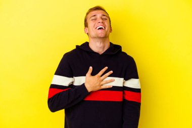Sarı arka planda izole edilmiş genç beyaz adam yüksek sesle gülüyor ve elini göğsüne koyuyor..