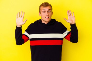 Sarı arka planda izole genç beyaz adam hoş bir sürpriz alıyor, heyecanlı ve el kaldırıyor..