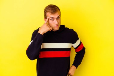 Sarı arka planda izole edilmiş genç beyaz bir adam şakağı parmağıyla işaret ediyor, düşünüyor ve bir göreve odaklanıyor..